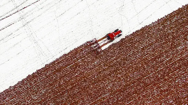 Photo of Aerial view of tractor tilling snow covered field in Winter