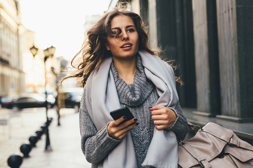 A young woman texting on the phone while rushing down the street.