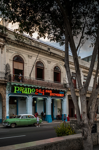 Havana, Cuba - October 12, 2016: Local restaurant Prado 264 in Old Havana, Cuba. People standing in front of the building, patrons sitting at the tables. Prado Boulevard is one of the major streets in downtown Havana, leading from Malecon shore line to Capitolio Parliament building. Typical scene all around old Havana, where ever you see old buildings . Variety of colours and styles. Beauty of old architecture neglected over many years with out upkeep.