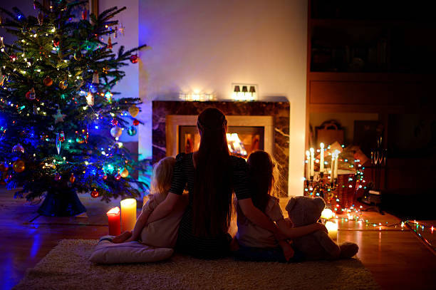 istock Young mother and daughters sitting by a fireplace on Christmas 628024002