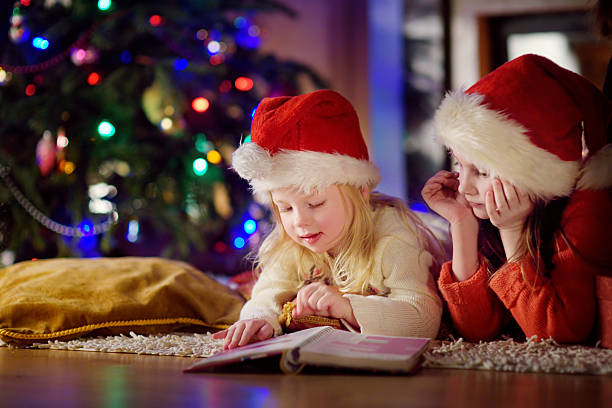 istock Two cute little sisters reading story book under Christmas tree 628024216