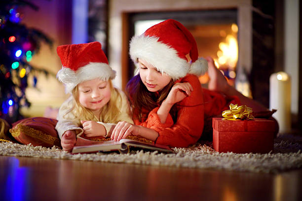 istock Two cute little sisters reading story book under Christmas tree 628025478
