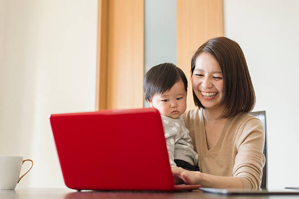 自宅で彼女の女の赤ちゃんと一緒に働く若い母親 - 日本人　親子 ストックフォトと画像