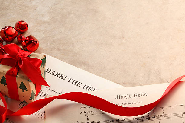 Small Present Resting On Christmas Sheet Music A small Christmas present is surrounded by a curled red ribbon and several red bells of differing sizes as its rests on top of the sheet music from several classic Christmas songs including Jingle Bells and Hark The Herald Angels Sing.  All music is within the public domain. chinese lantern lily photos stock pictures, royalty-free photos & images