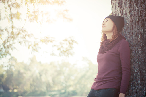 Happy beautiful woman leaning against a tree looking on the sky