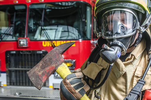 Headshot on fireman wearing full protection equipment and holding an axe in front of truck