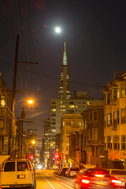 San Francisco, CA, USA - November 14, 2016: Transamerica Pyramid and supermoon on the background.Cable car rail in the front and pass through Washington Street. Some cars parked on the sides. 