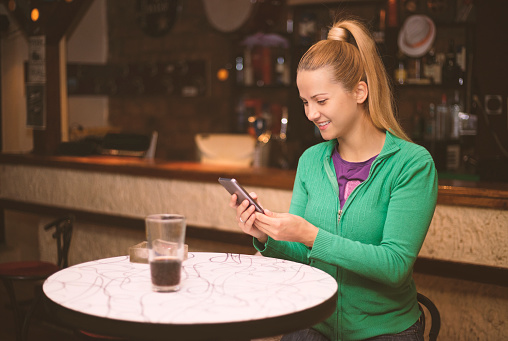 Woman in pub texting massage with smartphone