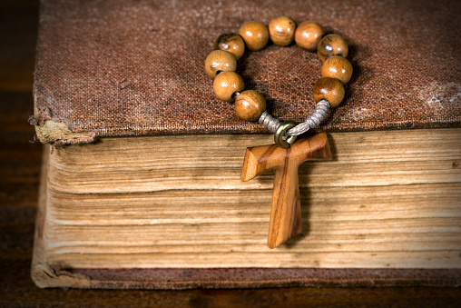 Tau, wooden cross in shape of the letter t (religious symbol of St. Francis of Assisi) with rosary bead on an old Holy Bible