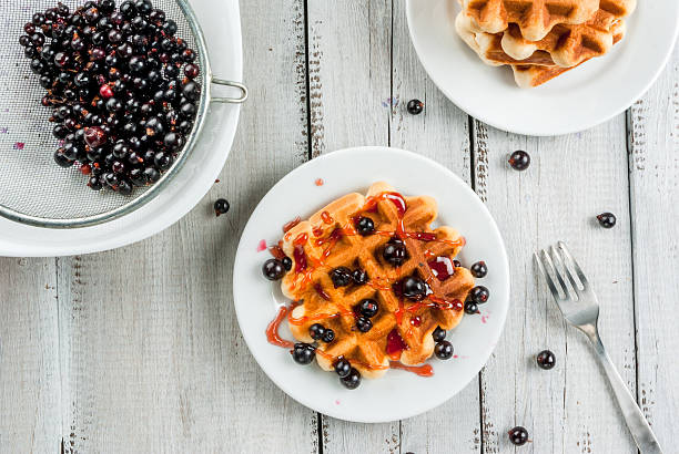 Homemade breakfast. Fresh Belgian waffles with summer berries and currant jam. On a white rustic wooden table.