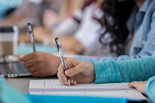 Close up of a female Caucasian high school or college student taking notes during class. She is writing in a spiral notebook.