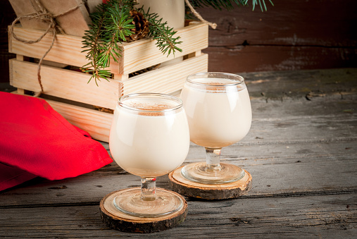 Traditional Christmas alcoholic cocktail - Irish Cream, Cola de mono (monkey tail), decorated with cinnamon. Against the background of Christmas decorations on a wooden table. Copy space