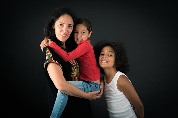 Cute little daughter with son and mother join hands in shape of heart as concept of mom and kids love care support, smiling mum and her kids looking at camera posing together for headshot portrait