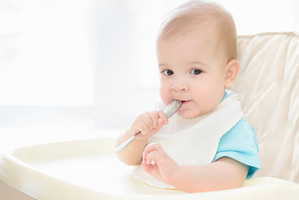 istock baby holding a spoon in his mouth 628096124