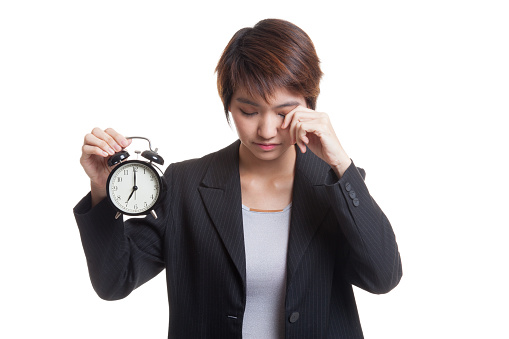 Sleepy young Asian business woman with a clock in the morning  isolated on white background.
