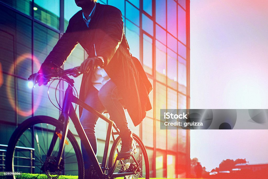 Handsome man riding bicycle beside the modern office building Handsome man, on the way to work, riding bicycle beside the modern office building. The man is casually dressed and wears eyeglasses and carries black briefcase hung on shoulder. Blurred motion, unrecognizable person, copy space has been left. City Stock Photo