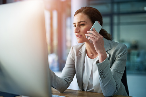 Shot of an attractive businesswoman answering her cellphone while sitting at her desk