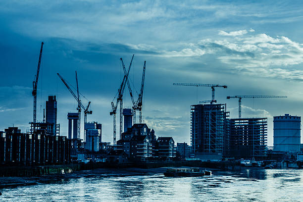 Wide angle image of cranes and other construction equipment busy at work developing London's ever-changing skyline - creating new housing and office space. In the foreground are the famous waters of the river Thames. Horizontal colour image with copy space.