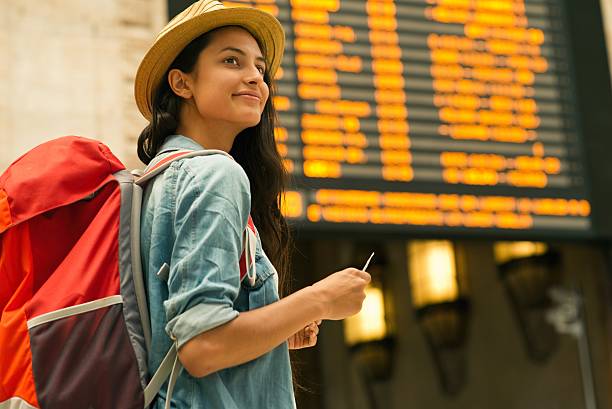 jeune femme vérifiant son train dans le tableau de temps - arrival airport airport lounge flying photos et images de collection