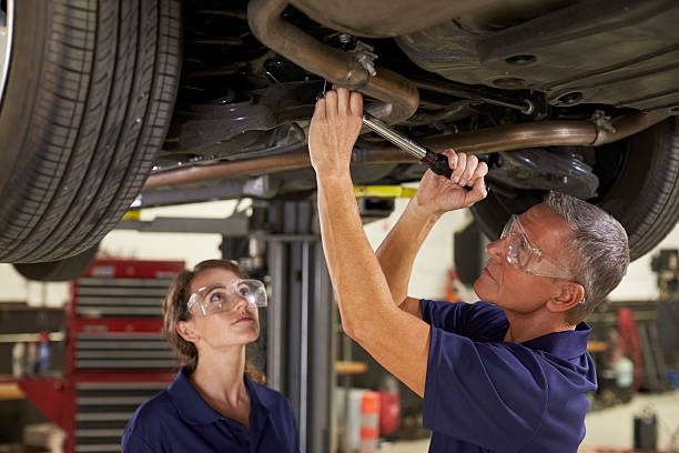 male and female mechanics working underneath car together - trainee working car mechanic imagens e fotografias de stock