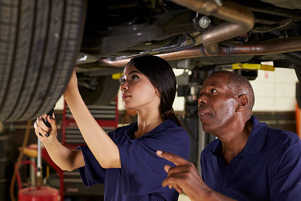 mechanic and female trainee working underneath car together - trainee working car mechanic imagens e fotografias de stock