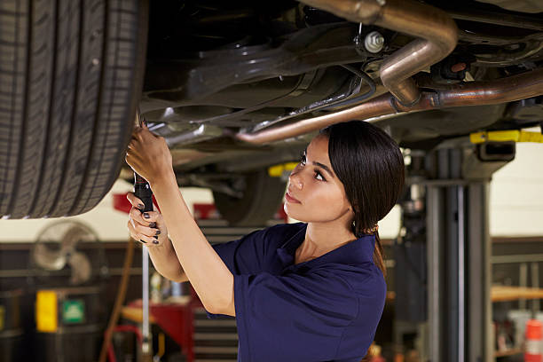 female auto mechanic working underneath car in garage - trainee working car mechanic imagens e fotografias de stock