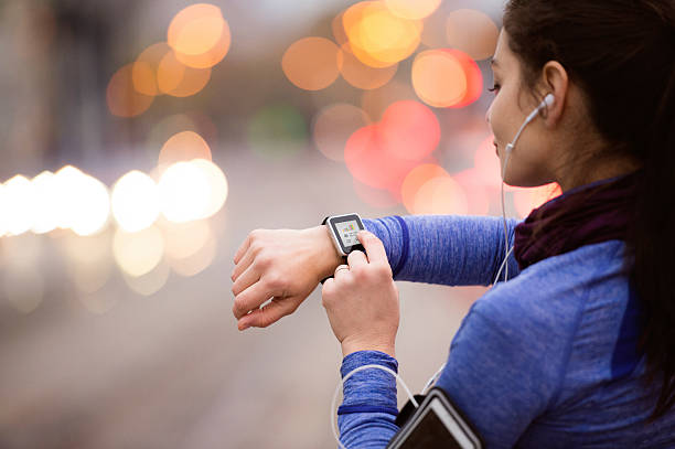 Young woman in blue sweatshirt running in the city Beautiful young woman in the city with smart phone, smartwatch and earphones, listening music. Using a fitness app for tracking weight loss progress, running goal or summary of her run. Rear view. smart watch stock pictures, royalty-free photos & images