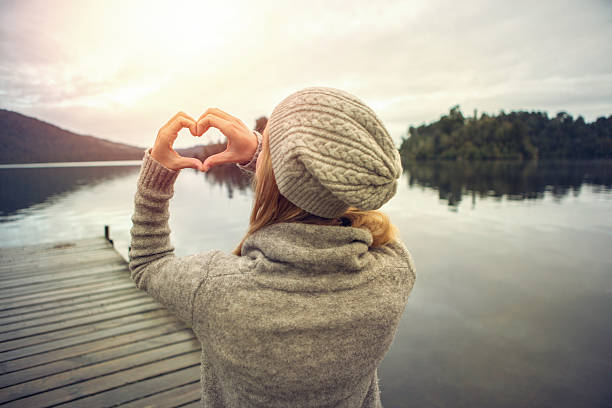 istock Young woman on lake pier, makes heart shape finger frame 628119536