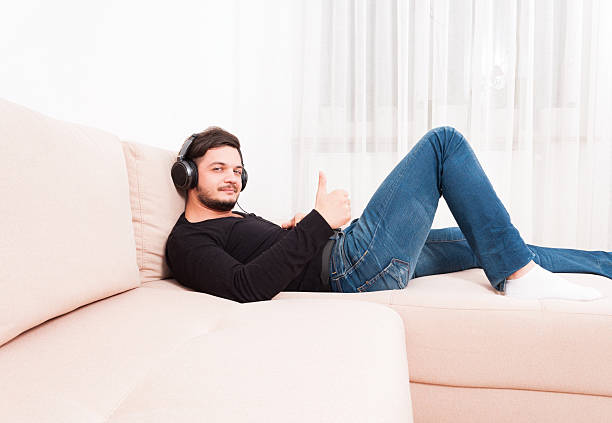 istock Man laying on sofa wearing headphones showing thumb up 628120088