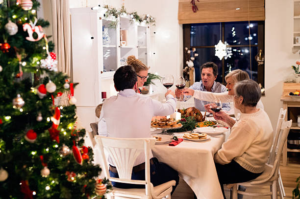 Beautiful big family celebrating Christmat together Beautiful big family sitting at the table, celebrating Christmat together at home. Illuminated Christmas tree behind them. big family table stock pictures, royalty-free photos & images