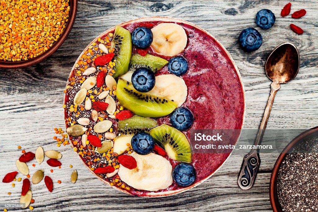 Acai breakfast superfoods smoothies bowl with chia seeds, bee pollen Acai breakfast superfoods smoothies bowl with chia seeds, bee pollen, goji berry toppings and fruits. Overhead, top view, flat lay Bowl Stock Photo