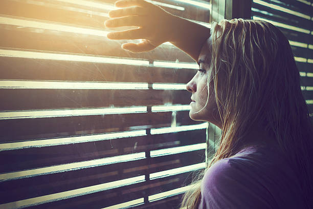 istock Sad and lonely blonde woman looking through window blinds 628134516