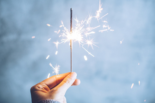 Close up of woman's hand holding sparklers on gray bakground.