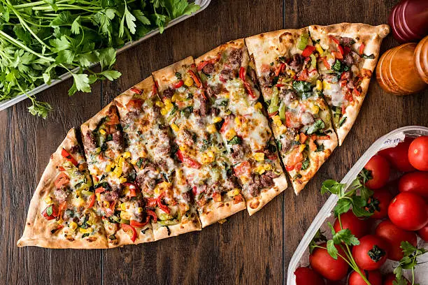 Turkish Pide with meat and vegetables on a wooden surface.