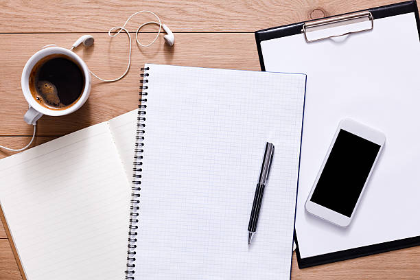 Notepad, diary, mobile phone and espresso coffee. Office or student's devices on modern wooden desk. Working table top view. Education or job background with copy space on paper sheet