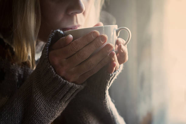 Woman in knitted sweater hands holding a cup warm coffee Woman in grey knitted sweater with traditional motifs drinking  a white cup of hot coffee with steam coming out in the morning light hot drink stock pictures, royalty-free photos & images