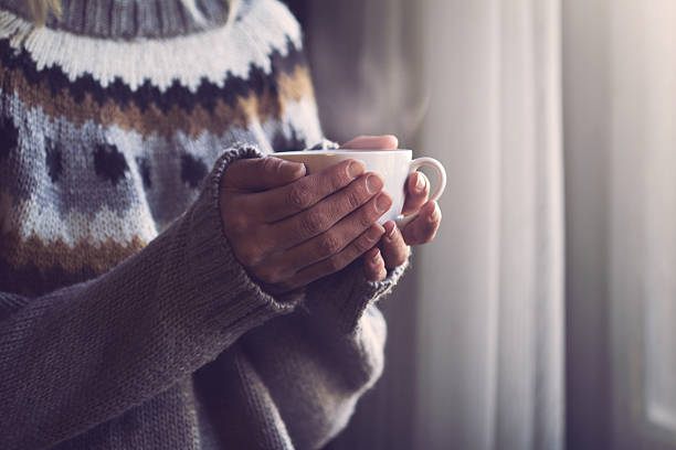 暖かいコーヒーのカップを持つニットセーターの手の女性 - human finger ストックフォトと画像