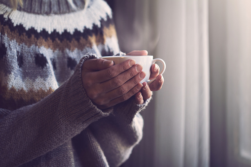 Woman in knitted sweater hands holding cup of warm coffee
