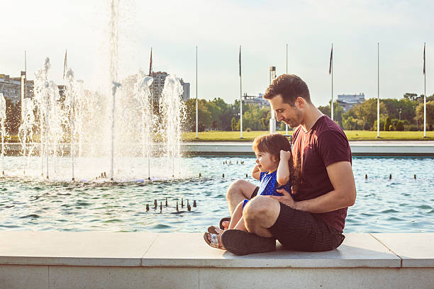 istock Father and daughter sitting by fountain 628164798