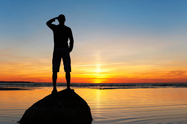 istock Young man silhouette standing on the rock at sunset background 628166252