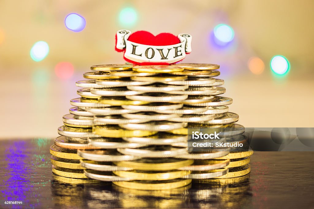 Pyramid of coins with the inscription love on top. Blurry Pyramid of coins with the inscription love on top. Blurry bright background with lights on a dark table Achievement Stock Photo