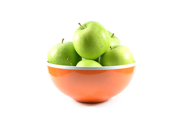 Green apples in orange bowl on white background.