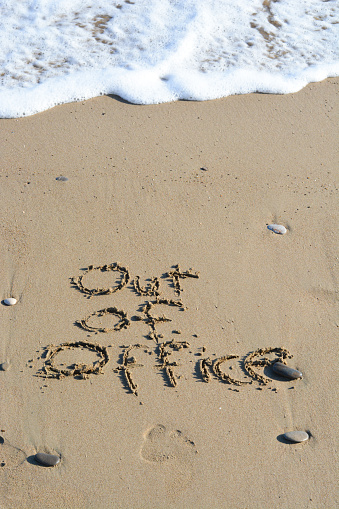 Out of office text written in sand on a beach suggesting work life balance