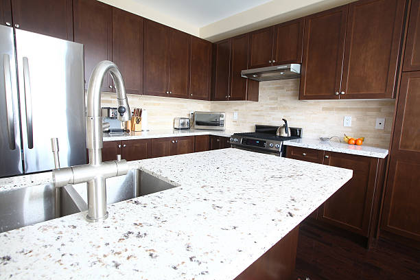 Domestic kitchen with quartz countertops and chestnut cabinets Modern kitchen with stainless steel appliances, limestone backsplash, quartz counter tops, chestnut color cabinetry, small appliances and goose-neck brushed nickel faucet. Kitchen design ideas. Kitchen concepts. Beautifully done kitchen with a very thoughtful design. Kitchen with an island design.  quartz stock pictures, royalty-free photos & images