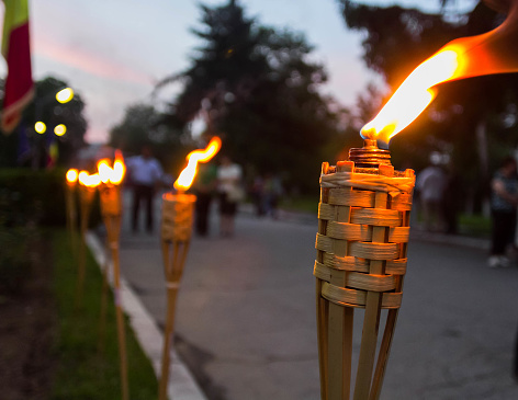 Closeup of flaming torches during an event. Blurred image of people and trees on the background