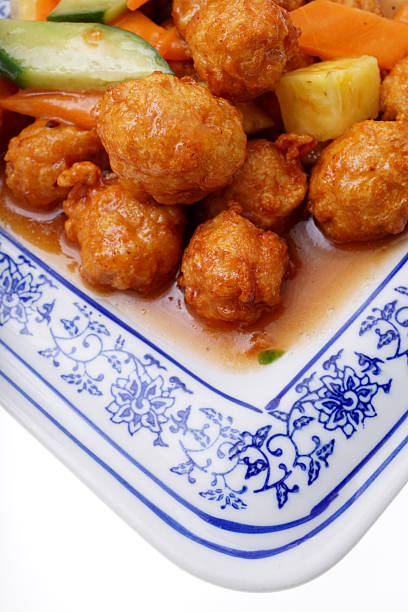 Chinese food. Sweet and sour chicken meatballs with pineapple in white plate isolated on white. Closeup.