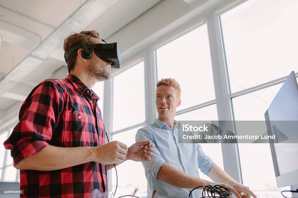 Developers testing an virtual reality device Shot of two young men testing virtual reality headset. Business men in office testing VR glasses. Leisure Games Stock Photo