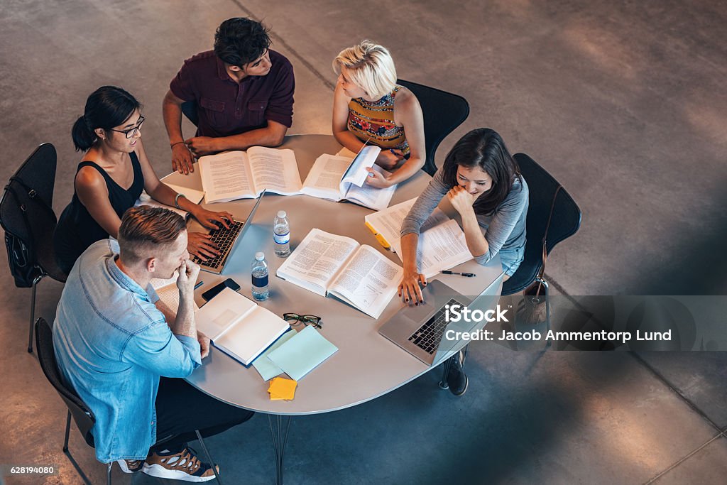 Mixed race students studying together Mixed race students sitting at table with books and laptop studying together. University Student Stock Photo