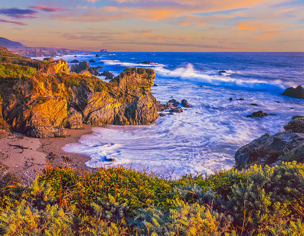 Dusk light casts a warm glow to a cove with breaking surf along the southern Big Sur coast, California