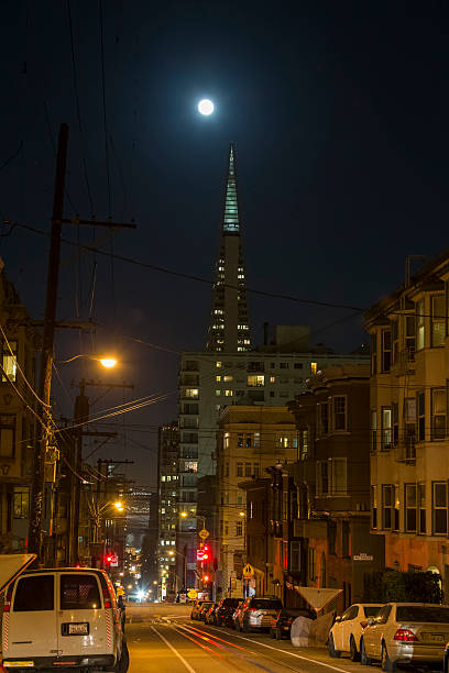 San Francisco, CA, USA - November 14, 2016: Transamerica Pyramid and supermoon on the background.Cable car rail in the front and pass through Washington Street. Some cars parked on the sides. 